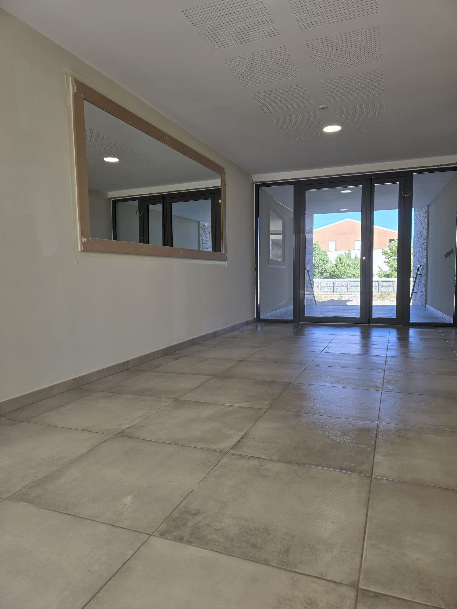 Séjour neuf au grand carrelage, baie vitrée et plafond acoustique